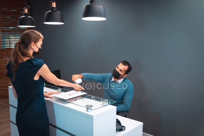 Two diverse businesspeople wearing face masks and taking temperature at reception. work at a modern office during covid 19 coronavirus pandemic. — Stock Photo