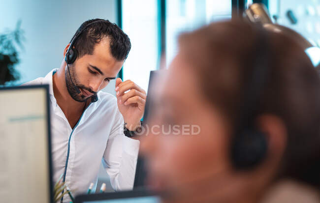 Змішаний гоночний бізнесмен носить гарнітуру і сидить за столом з колегами на задньому плані. робота в сучасному офісі . — стокове фото