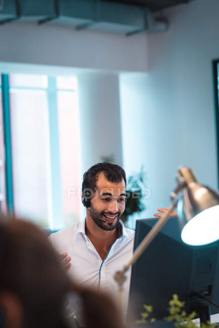 Mixed race businessman wearing headset and sitting at table with colleagues in background. work at a modern office. — Stock Photo
