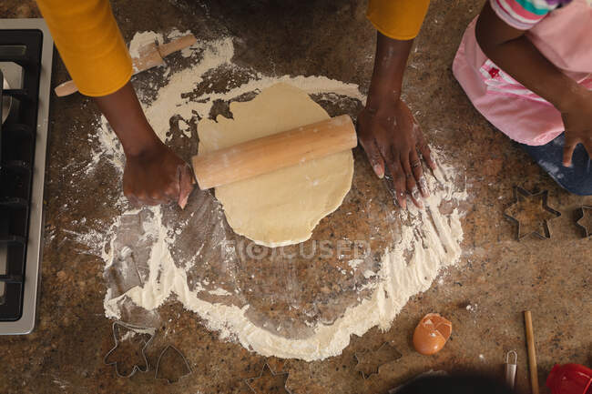 Angle élevé de la mère afro-américaine et sa fille qui cuisinent ensemble dans la pâte à rouler de la cuisine. passer du temps ensemble à la maison. — Photo de stock