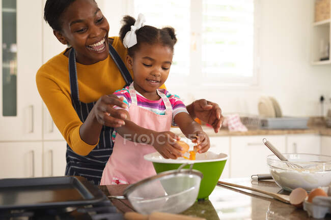 Улыбающиеся африканская американская мать и дочь веселятся на кухне, пекая вместе. Семья проводит время вместе дома. — стоковое фото