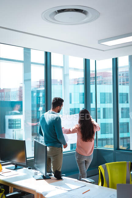 Dos empresarios diversos discutiendo juntos y sosteniendo esquema en ventana. trabajar en una oficina moderna. - foto de stock