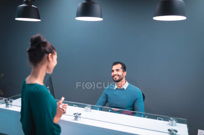 Dos empresarios diversos sonriendo y sentados en la mesa de cristal en la recepción. trabajar en un negocio creativo independiente. - foto de stock