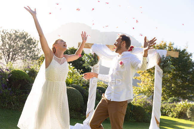 Felici sposi caucasici che si sposano, alzando le mani. matrimonio estivo, matrimonio, amore e concetto di celebrazione. — Foto stock