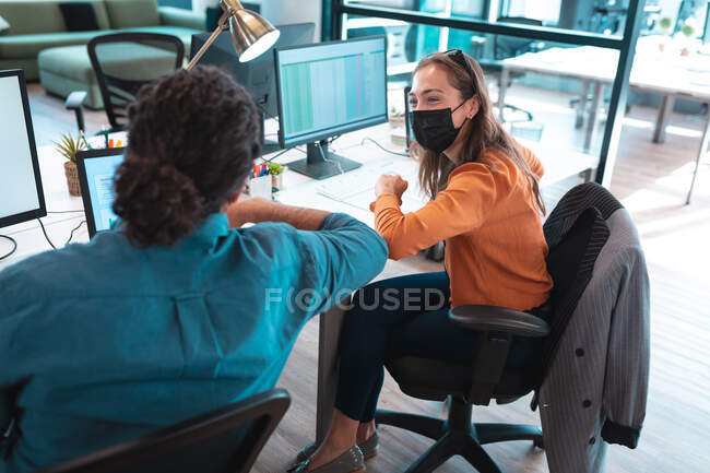 Zwei unterschiedliche Geschäftsleute mit Gesichtsmaske bedienen sich eines Computers. Arbeit in einem modernen Büro während der Covid 19 Coronavirus-Pandemie. — Stockfoto