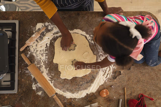 Alto ángulo de madre e hija afroamericana en formas de corte de cocina en masa juntos. familia pasar tiempo juntos en casa. - foto de stock
