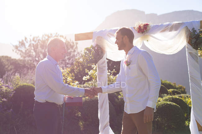 Novio caucásico casarse y darse la mano con oficiante de la boda. boda de verano, matrimonio, amor y concepto de celebración. - foto de stock