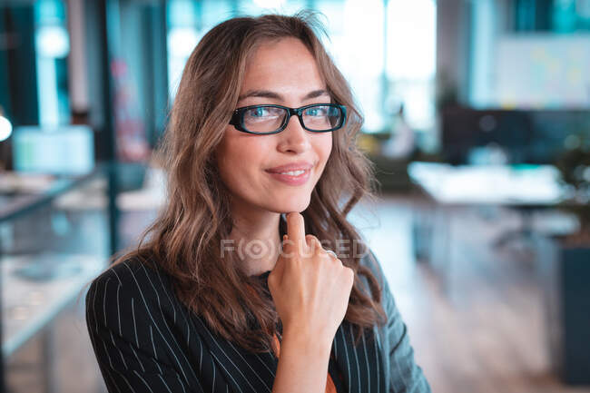 Портрет кавказької бізнес-леді, яка посміхається і дивиться на камеру з колегами на задньому плані. робота в сучасному офісі . — стокове фото