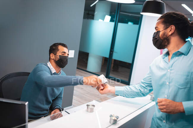 Two diverse businessmen wearing face masks at reception. work at a modern office during covid 19 coronavirus pandemic. — Stock Photo