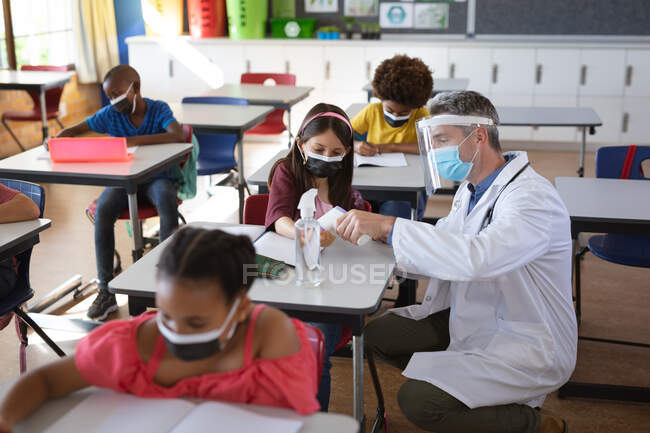 Kaukasischer Arzt mit Gesichtsschild, der in der Schule die Temperatur eines kaukasischen Mädchens misst. Gesundheitsschutz und Sicherheit in der Schule während des Covid-19-Pandemiekonzepts — Stockfoto