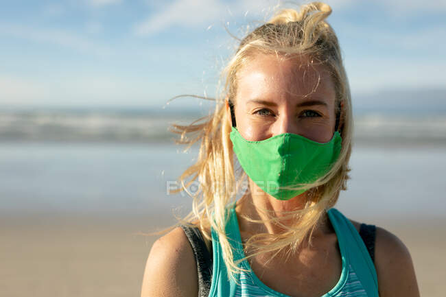 Retrato de mulher caucasiana usando máscara facial praticando ioga, de pé na praia. estilo de vida ativo saudável, aptidão ao ar livre e bem-estar durante a pandemia covid 19. — Fotografia de Stock