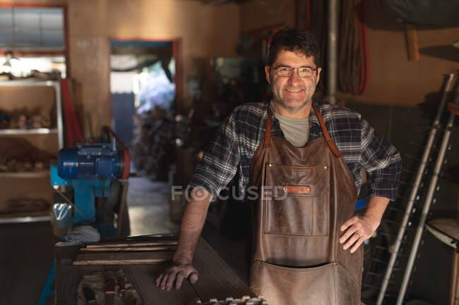 Smiling caucasian male knife maker in workshop looking at camera. independent small business craftsman at work. — Stock Photo