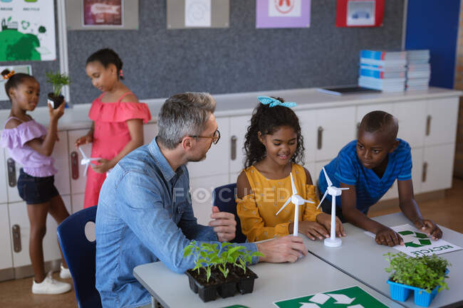 Кавказский учитель мужского пола держит модель ветряной мельницы, обучая мальчика и девочку в классе окружающей среды в школе. школа и концепция образования — стоковое фото