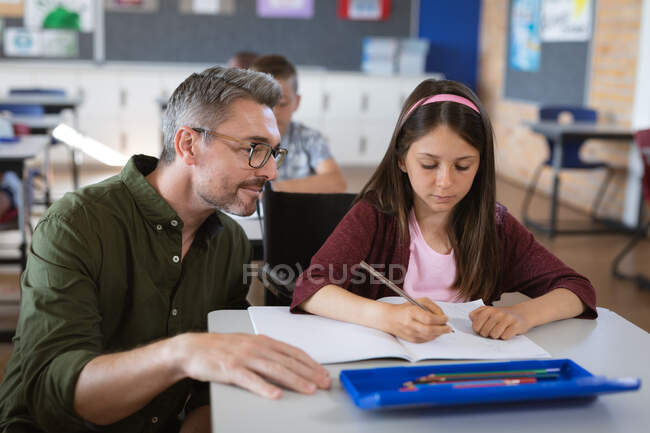 Caucásico maestro masculino enseñando chica caucásica en la clase en la escuela. escuela y concepto de educación - foto de stock