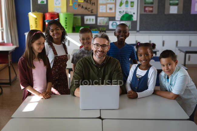 Retrato de un maestro caucásico y un grupo de estudiantes diversos con portátil en la clase en la escuela. escuela y concepto de educación - foto de stock