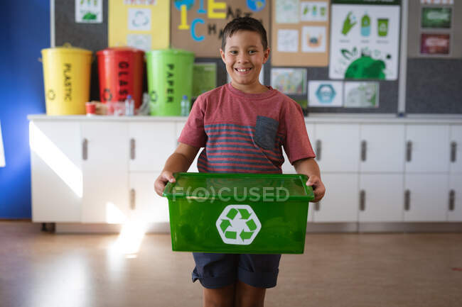 Portrait of caucasian boy smiling while holding tray filled with recyclable plastic items at school. school and education concept — Stock Photo