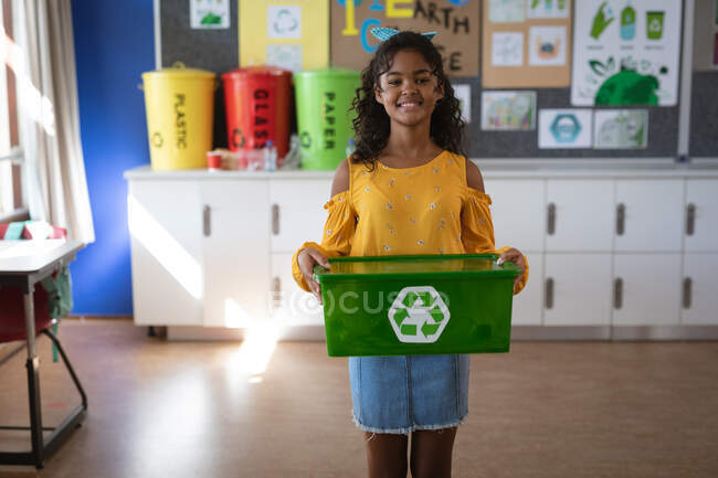 Retrato de menina afro-americana segurando bandeja cheia de itens de plástico reciclável na escola. conceito de escola e educação — Fotografia de Stock