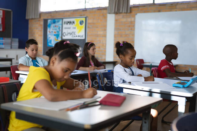 Група різноманітних студентів, які навчаються, сидячи на своїх столах у класі в школі. концепція школи та освіти — стокове фото