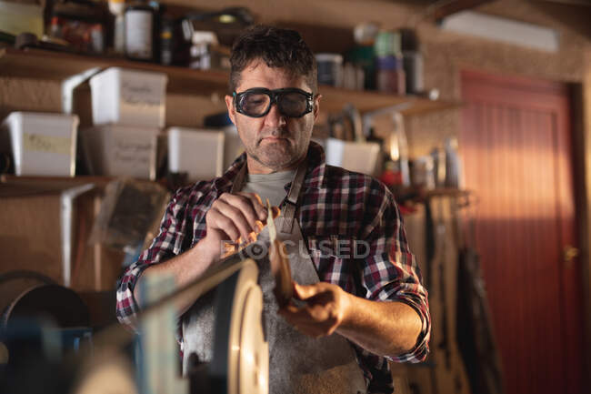 Fabricante de cuchillo masculino caucásico con delantal y gafas, haciendo cuchillo en el taller. artesano independiente de la pequeña empresa en el trabajo. - foto de stock