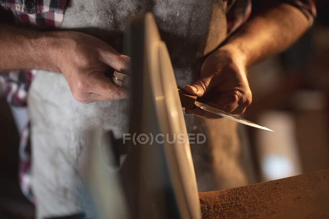 Manos de fabricante de cuchillos masculino usando delantal, haciendo cuchillo en el taller. artesano independiente de la pequeña empresa en el trabajo. - foto de stock