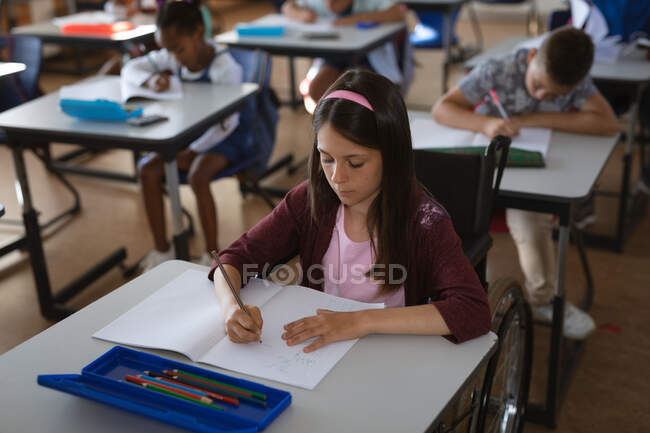 Chica caucásica estudiando mientras está sentada en su escritorio en la clase de la escuela. escuela y concepto de educación - foto de stock
