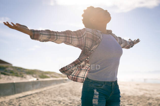 Heureuse femme afro-américaine qui s'amuse, debout sur la plage à bras ouverts. vacances, liberté et loisirs en plein air. — Photo de stock