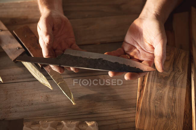 Hände eines kaukasischen Messermachers in der Werkstatt, der ein handgefertigtes Messer in der Hand hält. unabhängiger Kleinunternehmer bei der Arbeit. — Stockfoto