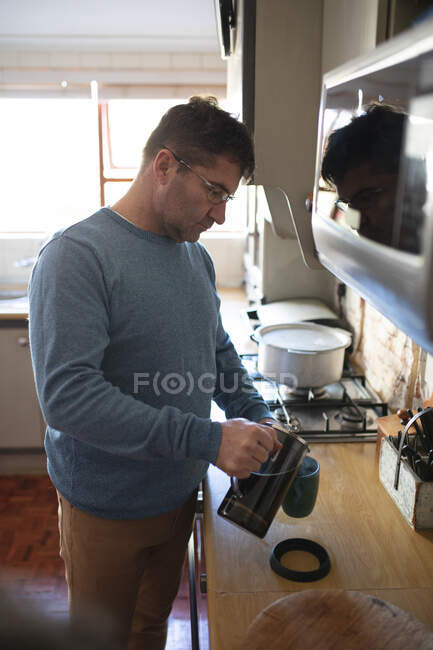 Кавказский мужчина стоит на кухне и готовит кофе с помощью французского пресса. проводить время дома. — стоковое фото