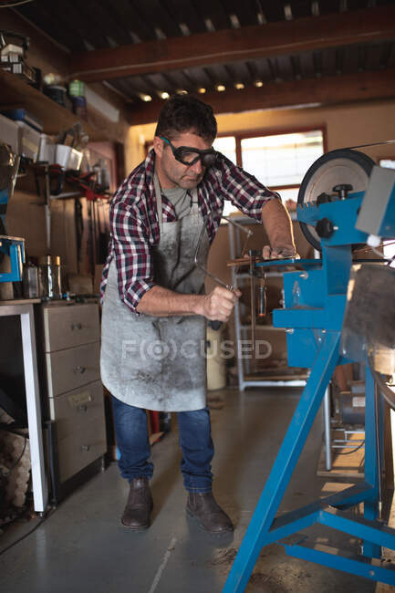 Kaukasischer Messermacher mit Schürze und Brille, der Messer in der Werkstatt herstellt. unabhängiger Kleinunternehmer bei der Arbeit. — Stockfoto