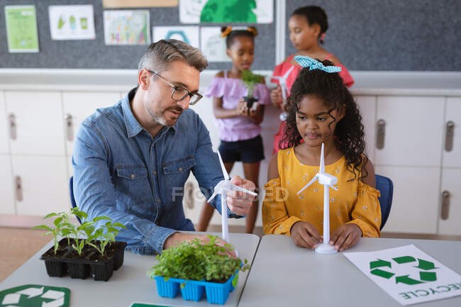 Caucasian male teacher holding windmill model teaching a girl during environment class at school. school and education concept — Stock Photo