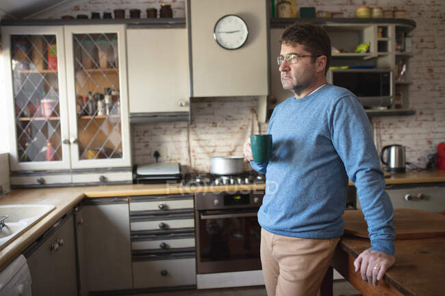 Focused caucasian man wearing glasses, standing in kitchen drinking coffee. spending free time at home. — Stock Photo