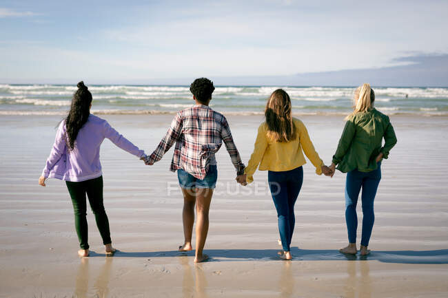 Grupo de diversas amigas cogidas de la mano, caminando por la playa. amigas unidas en la playa. - foto de stock