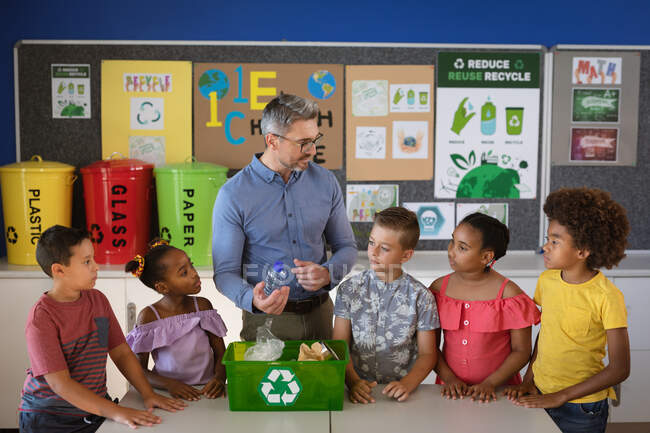 Caucasian male teacher teaching group of diverse students to recycle plastic items at school. school and education concept — Stock Photo