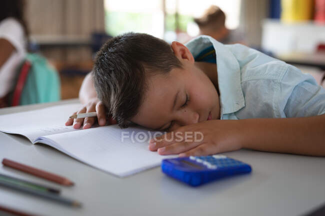 Garoto caucasiano dormindo em sua mesa na classe na escola. conceito de escola e educação — Fotografia de Stock