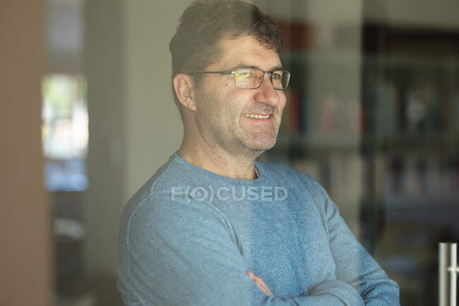 Retrato de un hombre caucásico sonriente con gafas mirando por la ventana. pasar tiempo libre en casa. - foto de stock