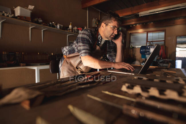 Faca masculina branca fabricante smartphone e laptop na oficina. artesão independente de pequenas empresas no trabalho. — Fotografia de Stock