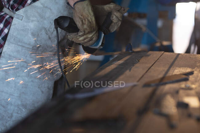 Hands of male knife maker wearing apron, using angle grinder in workshop. independent small business craftsman at work. — Stock Photo
