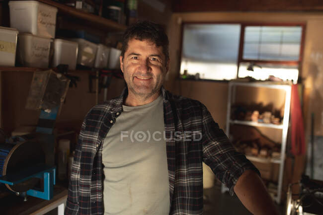 Sonriente fabricante de cuchillos masculino caucásico en el taller mirando a la cámara. artesano independiente de la pequeña empresa en el trabajo. - foto de stock