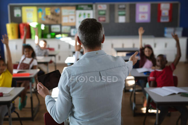 Visão traseira do professor masculino caucasiano usando tablet digital enquanto dava aulas na escola. conceito de escola e educação — Fotografia de Stock
