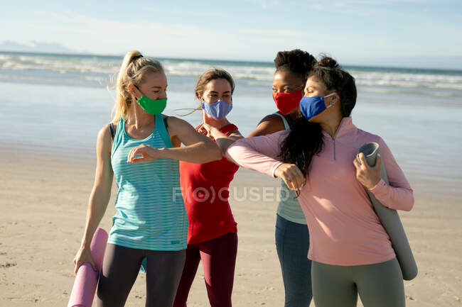 Gruppe verschiedener Freundinnen mit Gesichtsmaske, die Yoga praktizieren, im Stehen und am Strand. gesunder aktiver Lebensstil, Fitness und Wohlbefinden an der frischen Luft während der 19 Pandemie. — Stockfoto