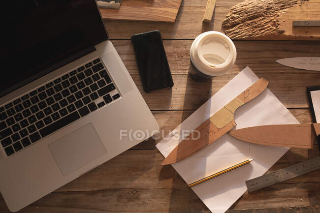 Laptop, smartphone, moldes de faca e outros utensílios deitados na mesa na oficina do fabricante de facas. artesão independente de pequenas empresas no trabalho. — Fotografia de Stock