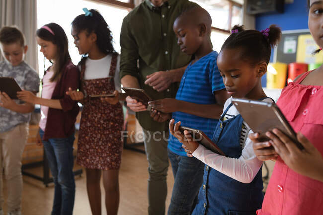 Caucasian male teacher and group of diverse students using digital tablets in the class at school. school and education concept — Stock Photo