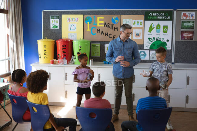 Белый мальчик и африканская американская девочка показывают, как перерабатывать пластиковые предметы для учеников в школе. школа и концепция образования — стоковое фото