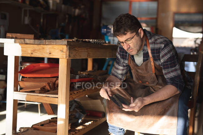 Caucasian male knife maker sitting at desk, analyzing knives in workshop. independent small business craftsman at work. — Stock Photo
