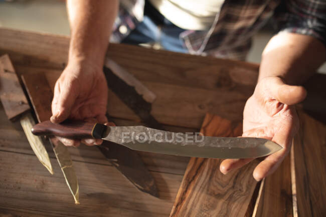 Hände eines männlichen Messermachers in der Werkstatt, der ein handgefertigtes Messer in der Hand hält. unabhängiger Kleinunternehmer bei der Arbeit. — Stockfoto