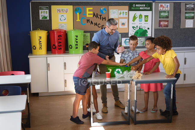 Professeur masculin caucasien et les élèves mettant des articles en plastique recyclable dans le plateau à l'école. concept scolaire et éducatif — Photo de stock