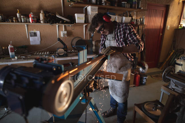 Kaukasischer Messermacher mit Schürze und Brille, der in der Werkstatt Schleifer verwendet. unabhängiger Kleinunternehmer bei der Arbeit. — Stockfoto
