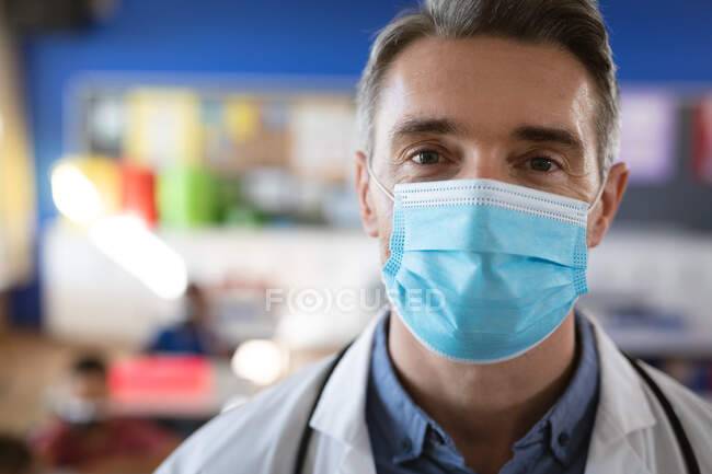 Retrato de médico caucasiano vestindo máscara facial na aula na escola. protecção da saúde e segurança na escola durante o conceito de pandemia de covid-19 — Fotografia de Stock