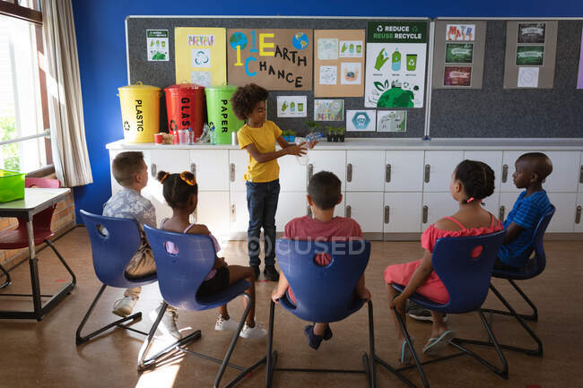 Menino afro-americano mostrando como reciclar itens de plástico para outros alunos da escola. conceito de escola e educação — Fotografia de Stock