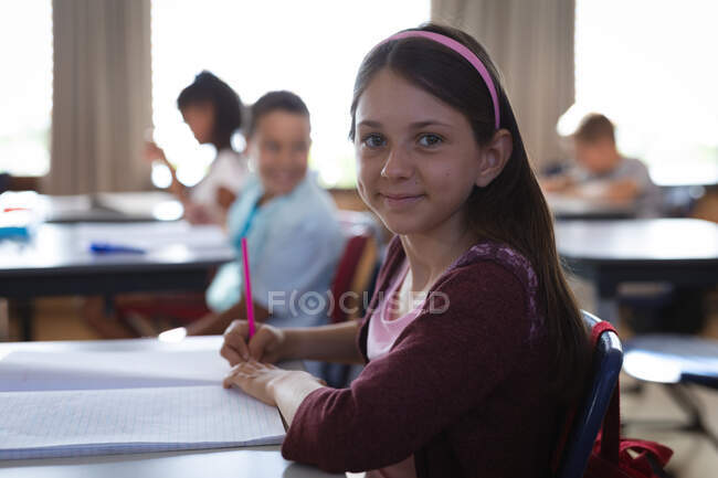 Porträt eines kaukasischen Mädchens, das in der Schulklasse auf ihrem Schreibtisch sitzt. Schul- und Bildungskonzept — Stockfoto